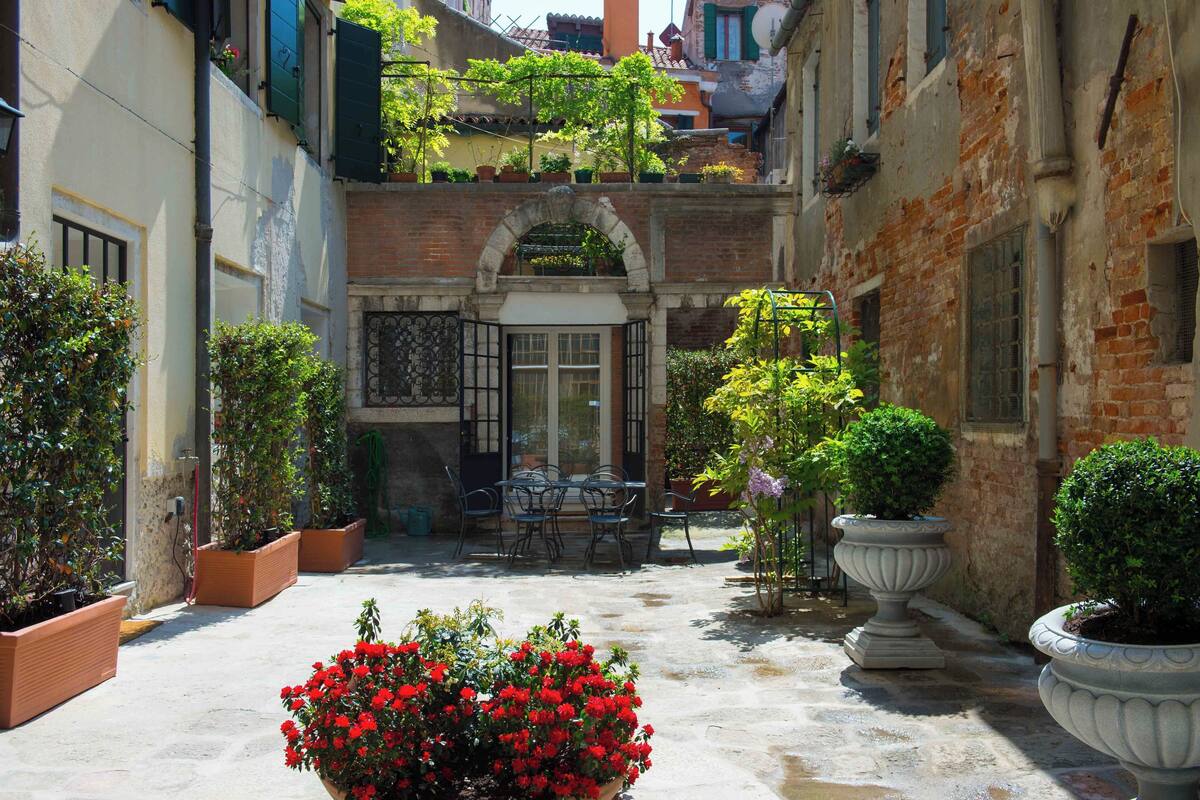 A courtyard with a table and chairs, potted plants, and a brick building.