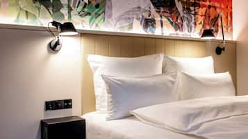 A hotel room with a bed, two bedside lamps, a control panel, and a colorful abstract wall art.