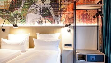 A hotel room with a bed, bedside lamps, a nightstand with a lamp, a small shelf, and a decorative wall with leaf patterns.