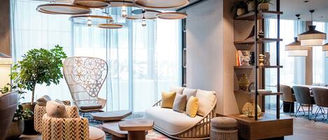 A modern interior with a sofa, chairs, a hanging light fixture, and a bookshelf.