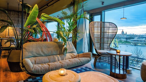 Un salon moderne avec un canapé, des fauteuils, une petite table et de grandes plantes en pot.