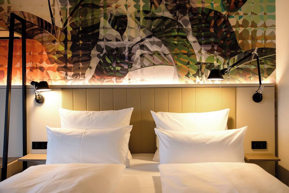 A hotel room with a bed, two bedside lamps, and a wall with a leaf-patterned design.