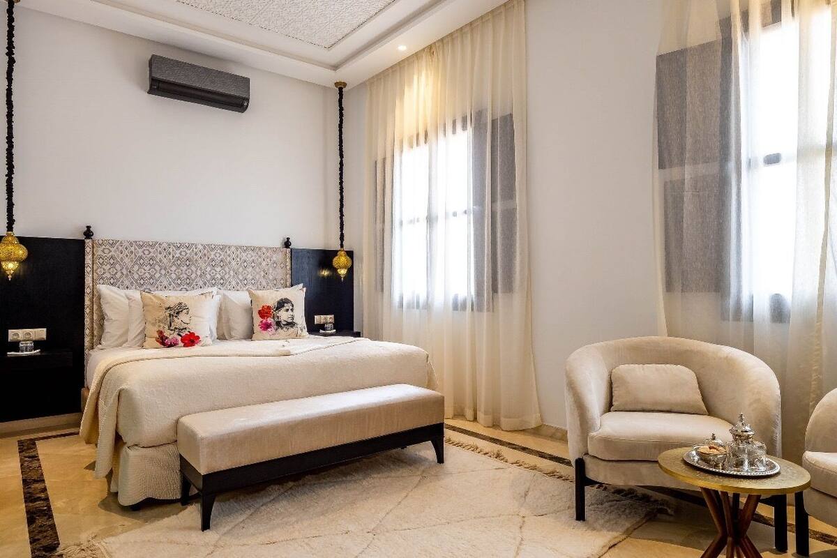 A bedroom with a bed, a bench, a chair, and a small table with a tray.