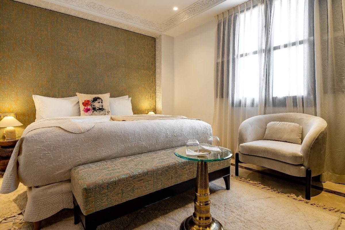 A bedroom with a large bed, a glass coffee table, a sofa, and a chair.