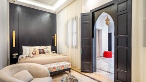 Un dormitorio con cama, mesita de noche y una silla. Hay una puerta que da a otra habitación.