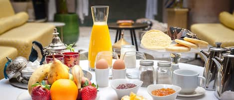 A breakfast table with fruits, pastries, and beverages, set in a well-lit room with yellow furniture and decorative items.