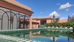 Una piscina con un diseño de baldosas a cuadros, rodeada por un edificio con techo de tejas y un ventanal grande.