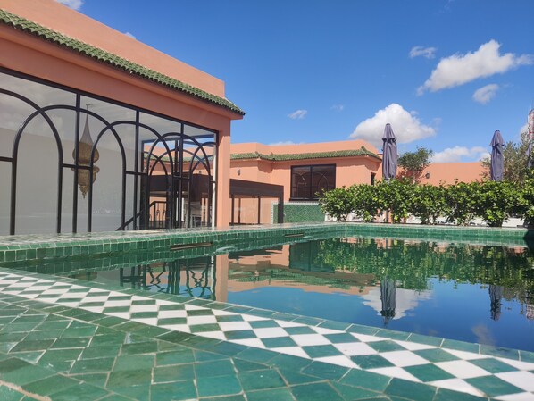 A swimming pool with a checkered tile pattern, surrounded by a building with a tiled roof and a large window.