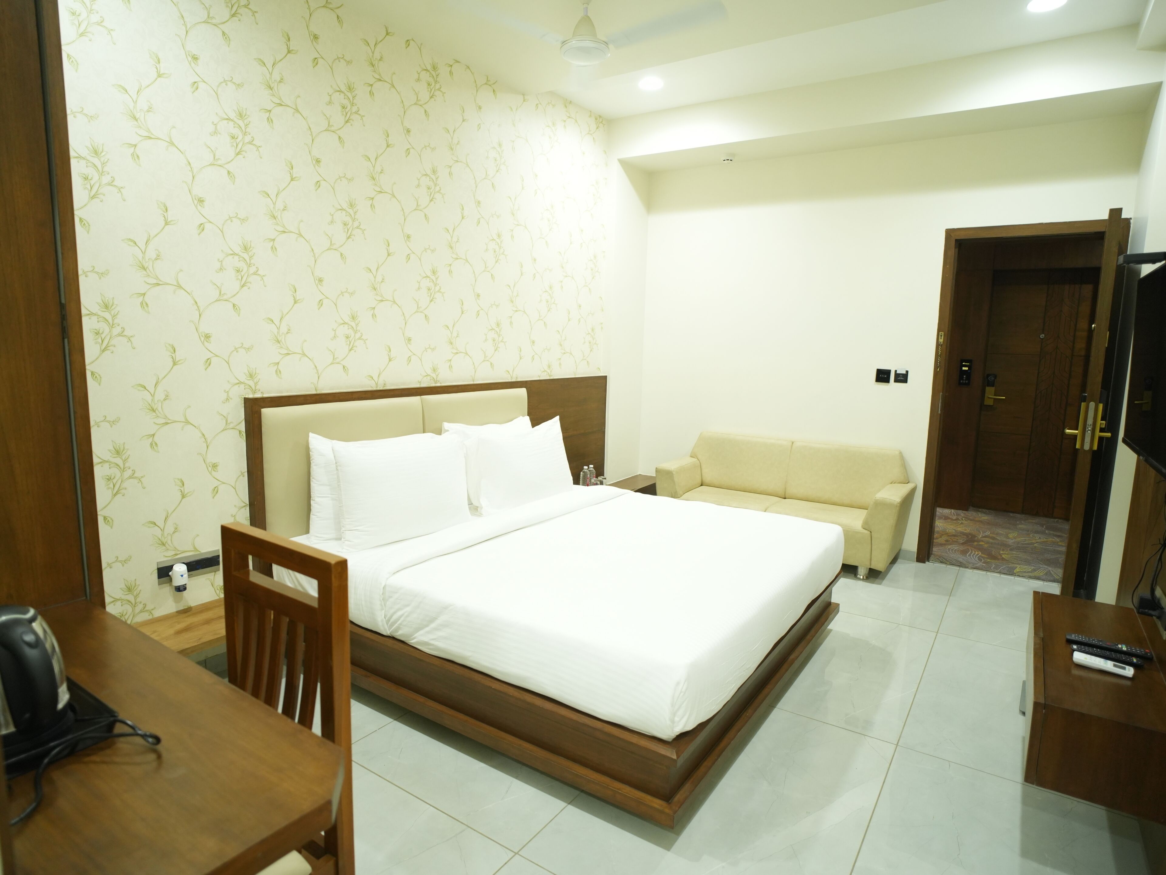 A hotel room with a large bed, a wooden headboard, a sofa, a desk with a chair, and a television.