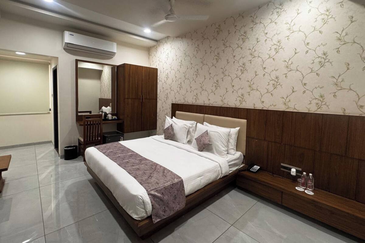 Een hotelkamer met een bed, een houten hoofdeinde, een spiegel, een kledingkast, een bureau en een badkamer.