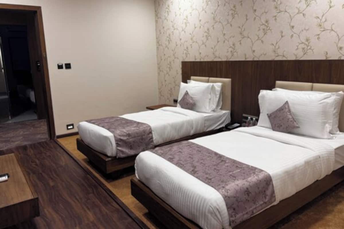 Een hotelkamer met twee bedden, een houten vloer, behang met een patroon en een kleine tafel.