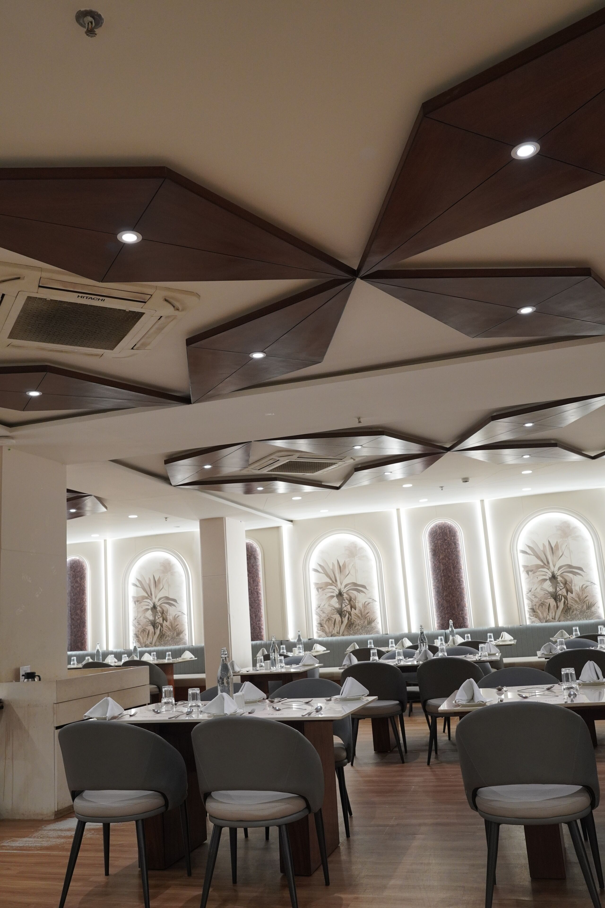A restaurant with a modern ceiling design, multiple dining tables, and chairs.