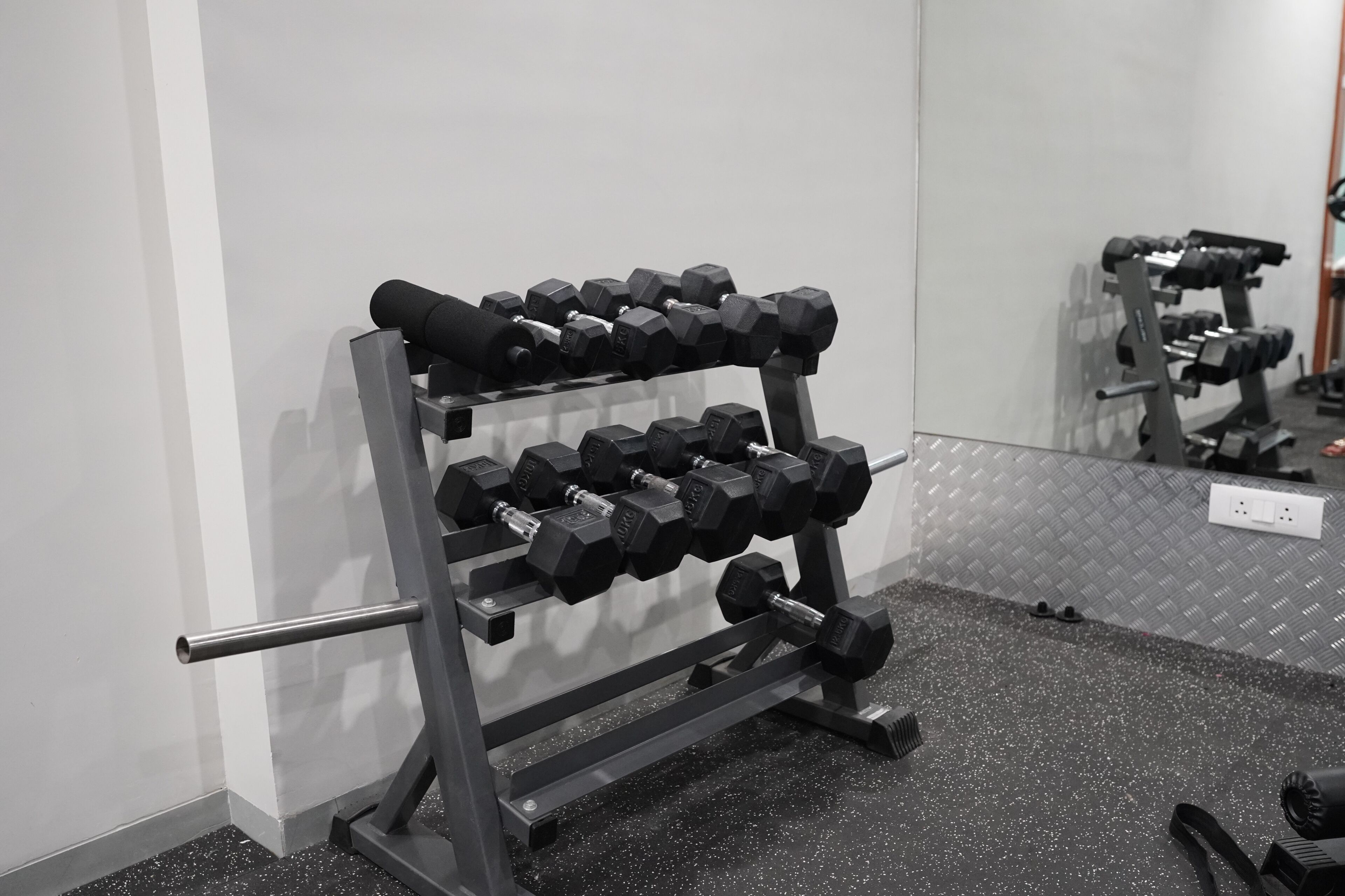 Uma academia com espelhos na parede, um suporte de metal com halteres e um piso salpicado.