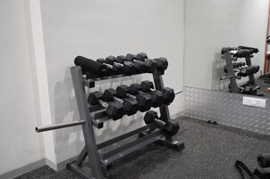 A gym with a mirrored wall, a metal rack holding dumbbells, and a speckled floor.