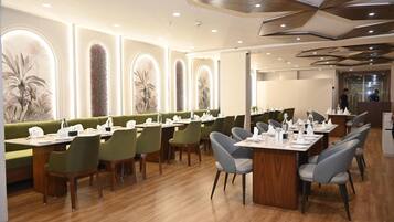 A modern restaurant with wooden tables, green and grey chairs, and a decorative ceiling.