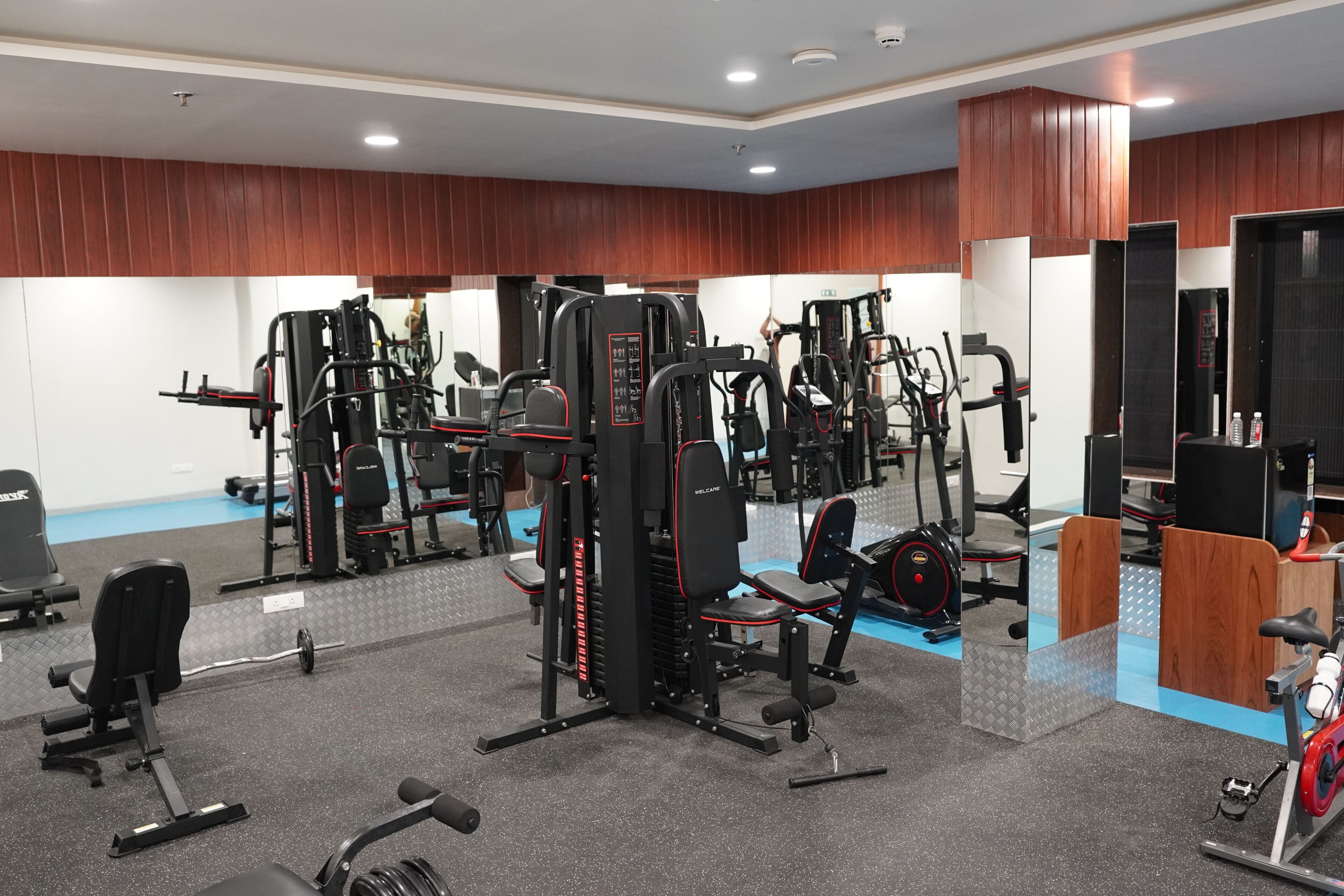 Ein Fitnessstudio mit verschiedenen Trainingsgeräten, Spiegeln und einer Holzwand.