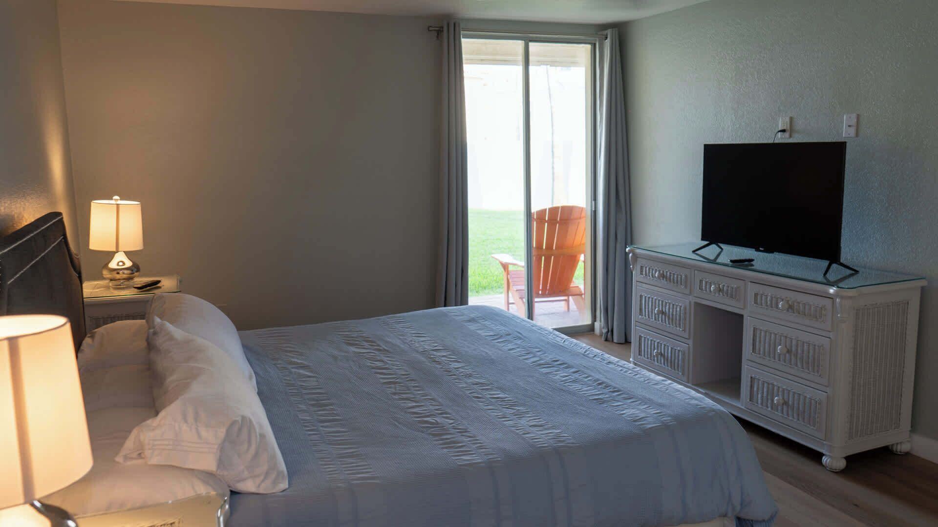 A hotel room with a bed, a television on a dresser, and a window with curtains.