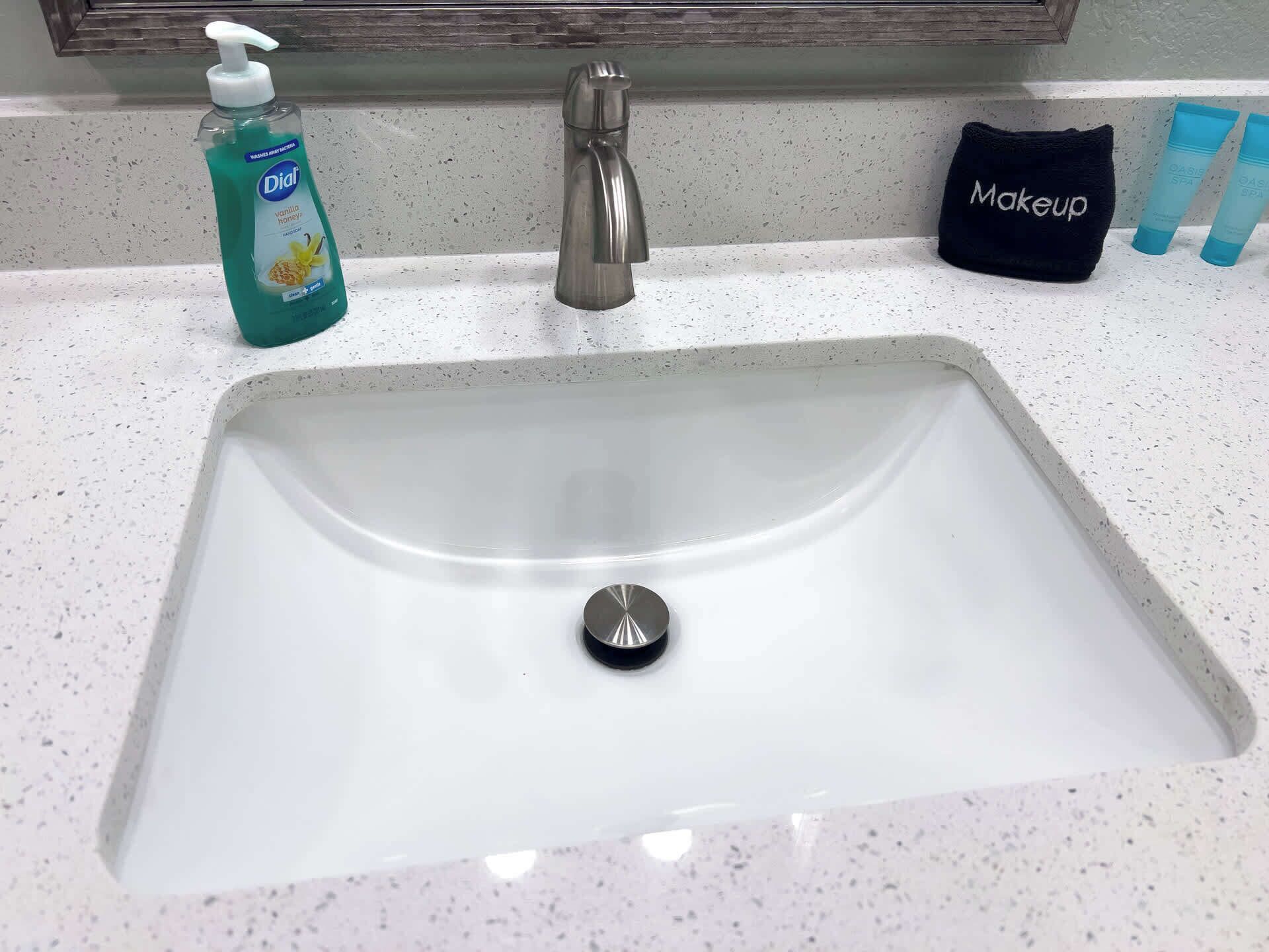 A bathroom sink with a soap dispenser, a makeup bag, and two toiletry bottles.