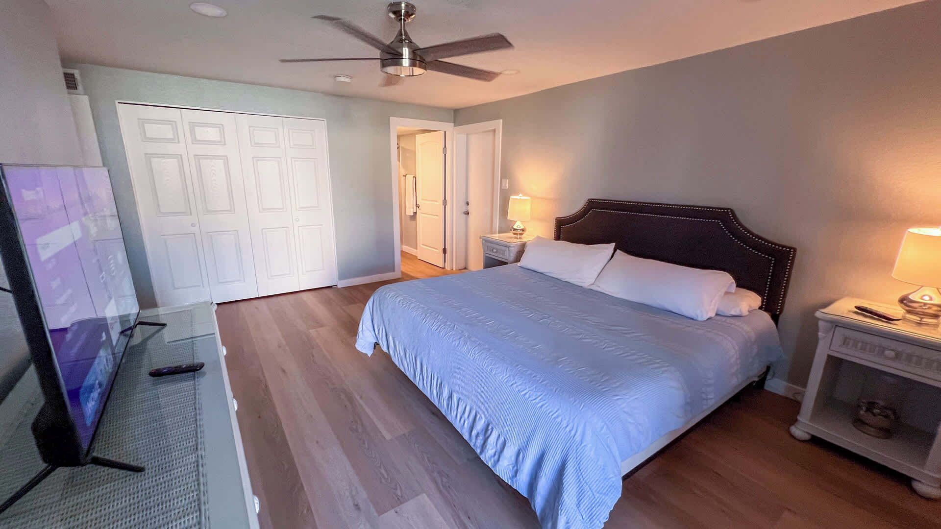 A bedroom with a bed, a nightstand, a ceiling fan, and a TV.