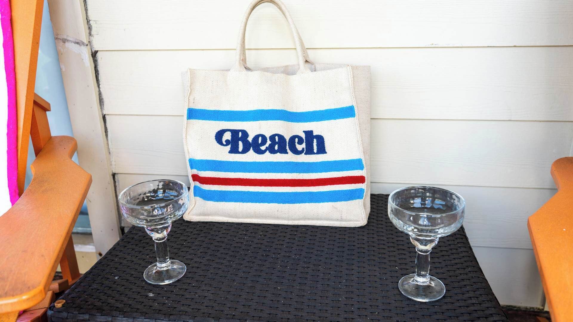A beach-themed tote bag with the word "Beach" on a table with two wine glasses.