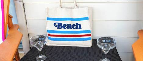 A beach-themed tote bag with the word "Beach" on a table with two wine glasses.
