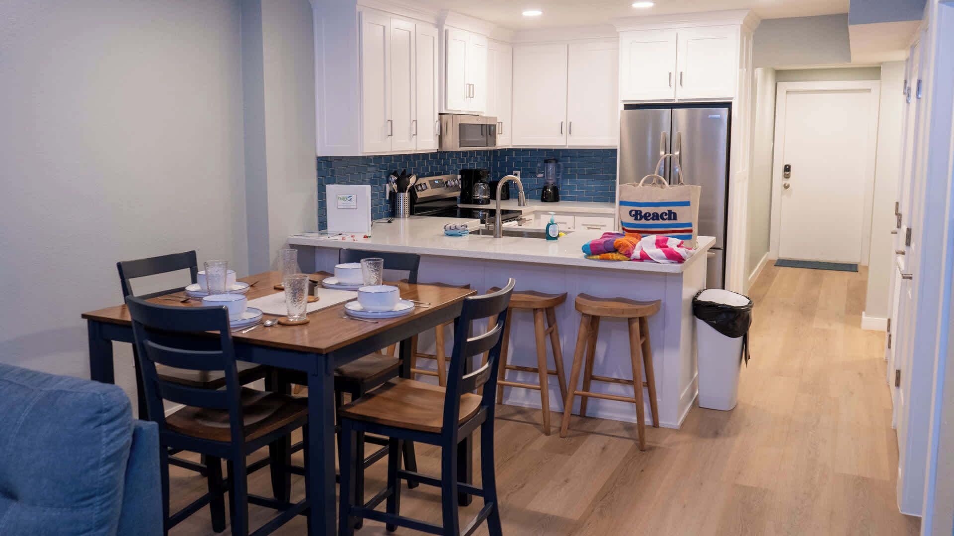 A compact kitchen with white cabinets, a stainless steel refrigerator, a coffee maker, and a blender on the counter.