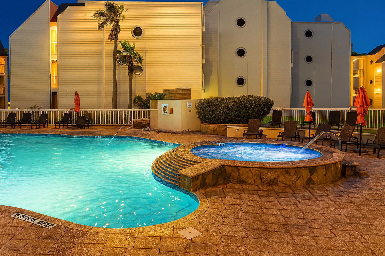 Una piscina con jacuzzi, sillas de descanso y sombrillas.