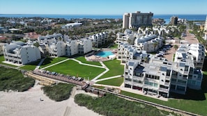Un hôtel situé sur la côte, composé de plusieurs bâtiments blancs, doté d’une piscine centrale et d’un espace aménagé sur la plage.