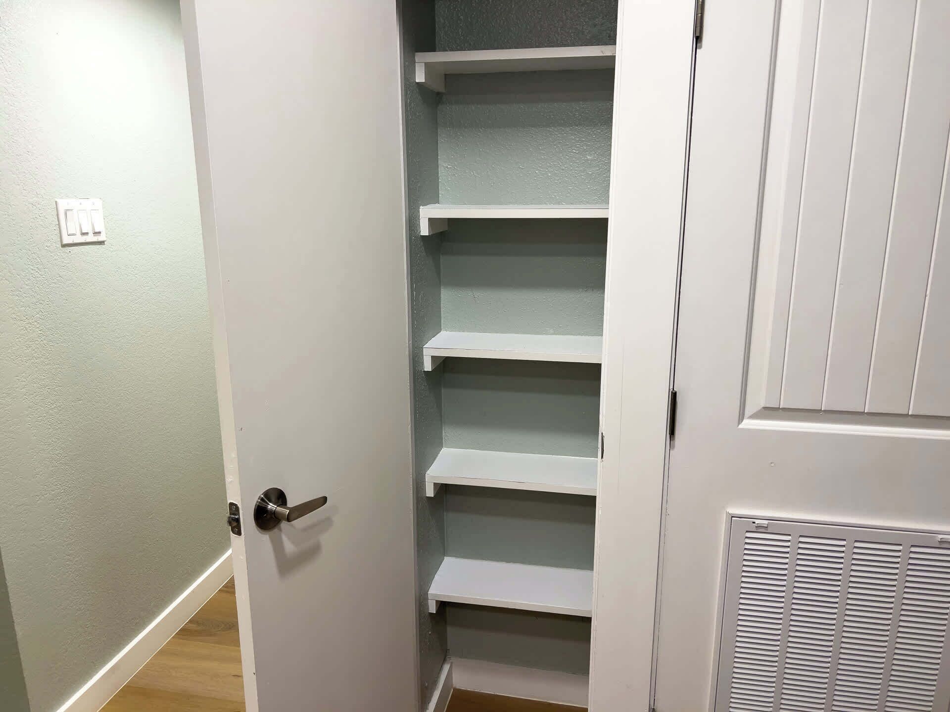 A closet with multiple shelves and a door with a handle.