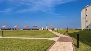 Una passeggiata di spiaggia con ombrelloni arancioni, una zona verdeggiante e un grande edificio sullo sfondo.