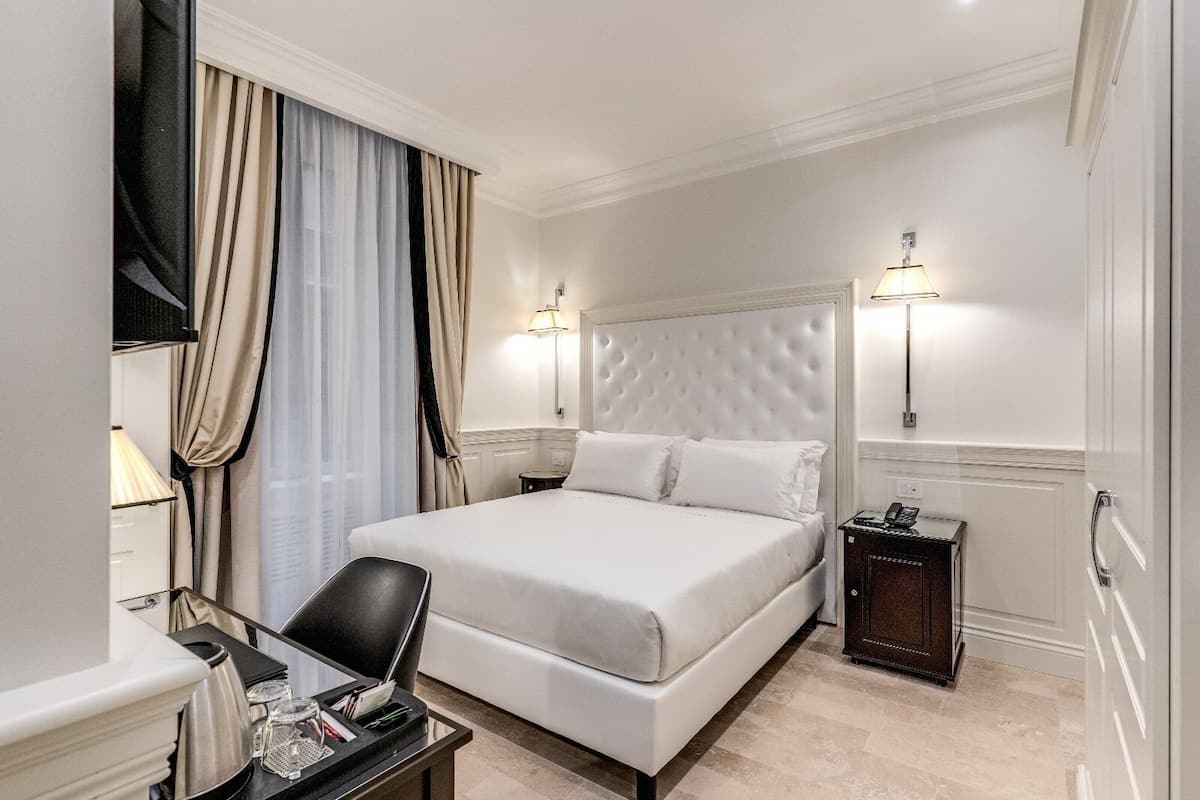 Una habitación de hotel con una cama grande, dos mesitas de noche, un escritorio con silla y una lámpara.