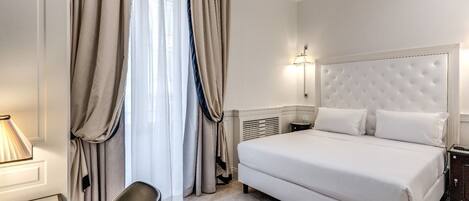 A hotel room with a large bed, a desk, a chair, a lamp, and a window with curtains.