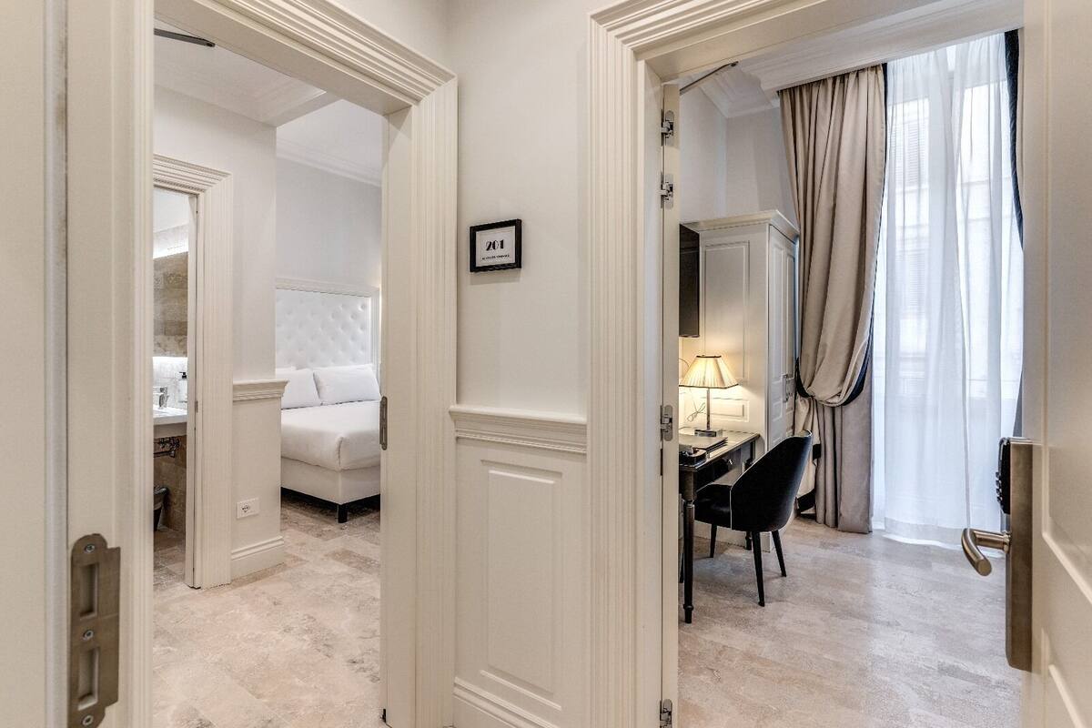 Una habitación de hotel con una cama, un escritorio con silla y una ventana con cortinas.