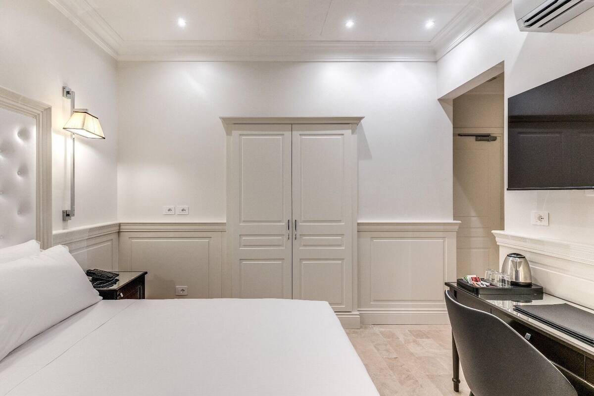 Habitación de hotel con una cama grande, un escritorio con silla, un armario y un televisor de pantalla plana montado en la pared.