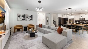 Una sala de estar moderna con un sofá seccional, una mesa de centro y un comedor con una cocina al fondo.