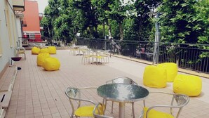 An outdoor patio with yellow chairs and tables, surrounded by a metal fence and trees. - HOTEL YOUNG PEOPLE UNDER 40 (Rimini)
