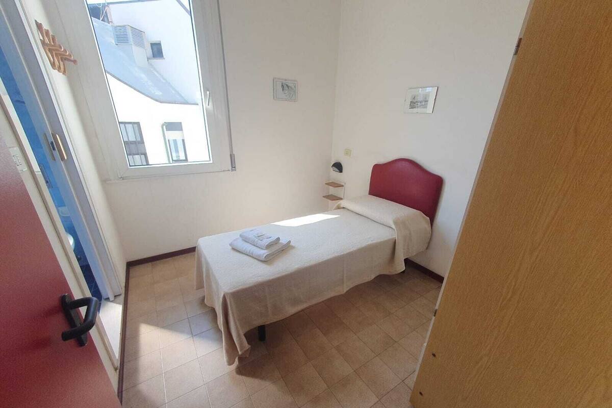 A small, single-bed room with a red headboard, a window, and a door.
