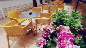 A patio area with yellow wicker chairs and tables, a tiled floor, and a potted plant with pink hydrangeas. - HOTEL YOUNG PEOPLE UNDER 40 (Rimini)