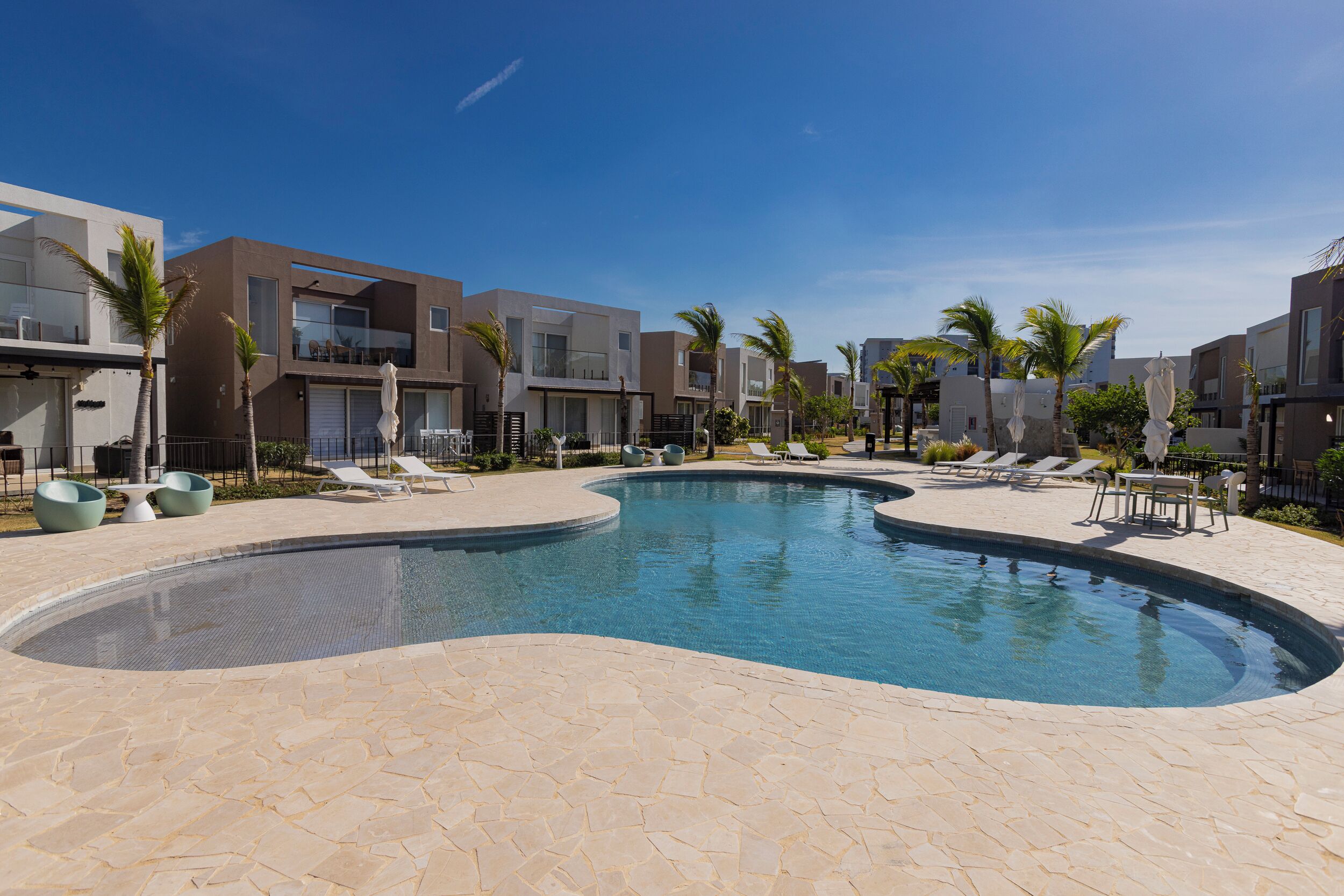 A swimming pool with a curved design, surrounded by modern buildings with balconies and palm trees.