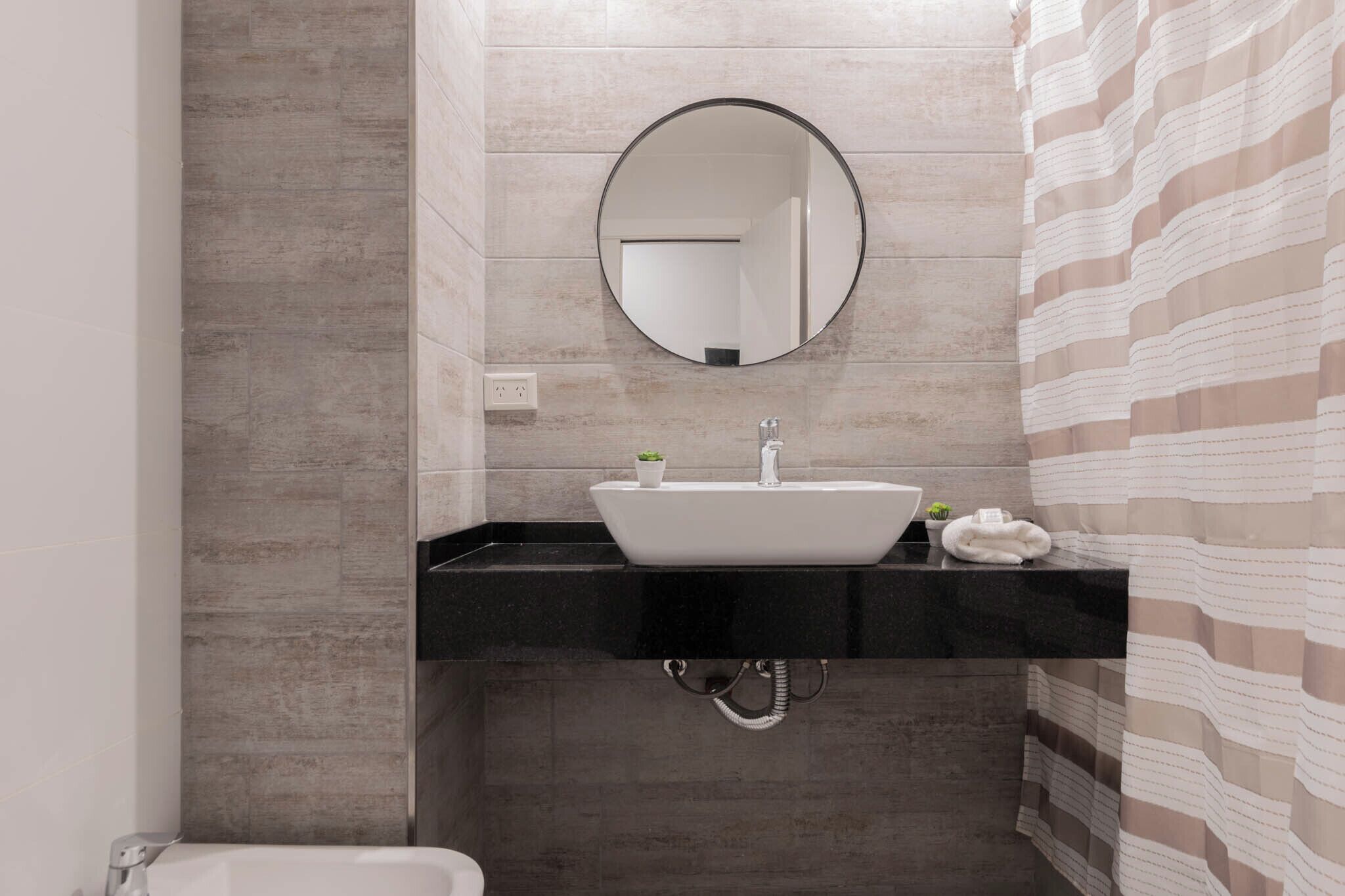 A bathroom with a white sink, a round mirror, and a striped shower curtain.
