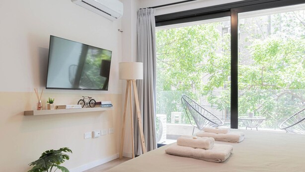 A modern hotel room with a large bed, a TV, a balcony with a view of greenery, and a small table with a chair. - MOT Azcuenaga 1800 (Buenos Aires)