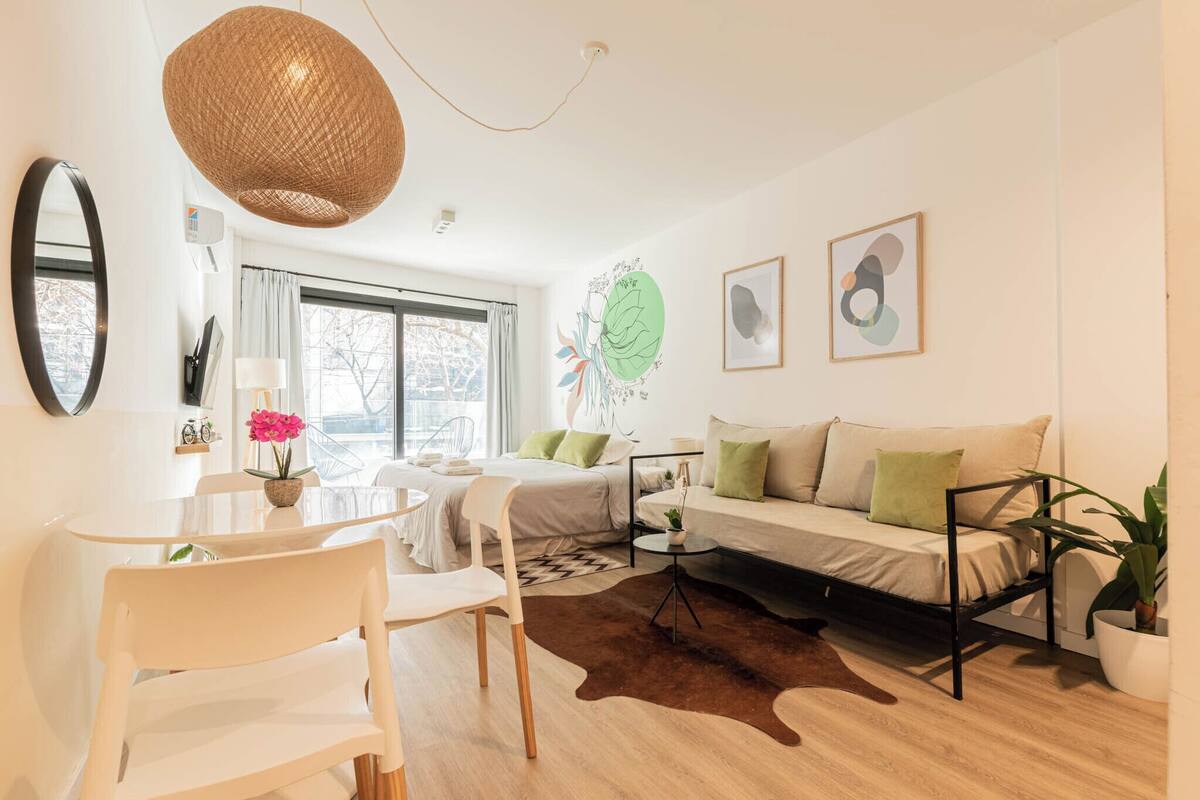 A modern living room with a sofa, chairs, a dining table, and a large window.