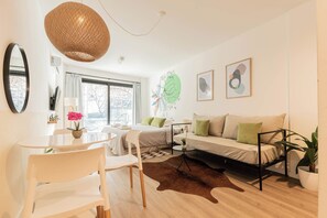 A modern living room with a sofa, chairs, a dining table, and a large window.