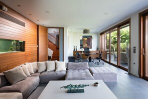 A modern living room with a sectional sofa, a white coffee table, and a large window. - Villa Terra Creta Luxury Retreat and Spa (Chania)