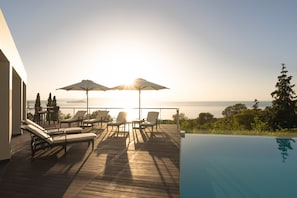 Une terrasse en bois avec des chaises longues et des parasols, donnant sur une étendue d’eau.