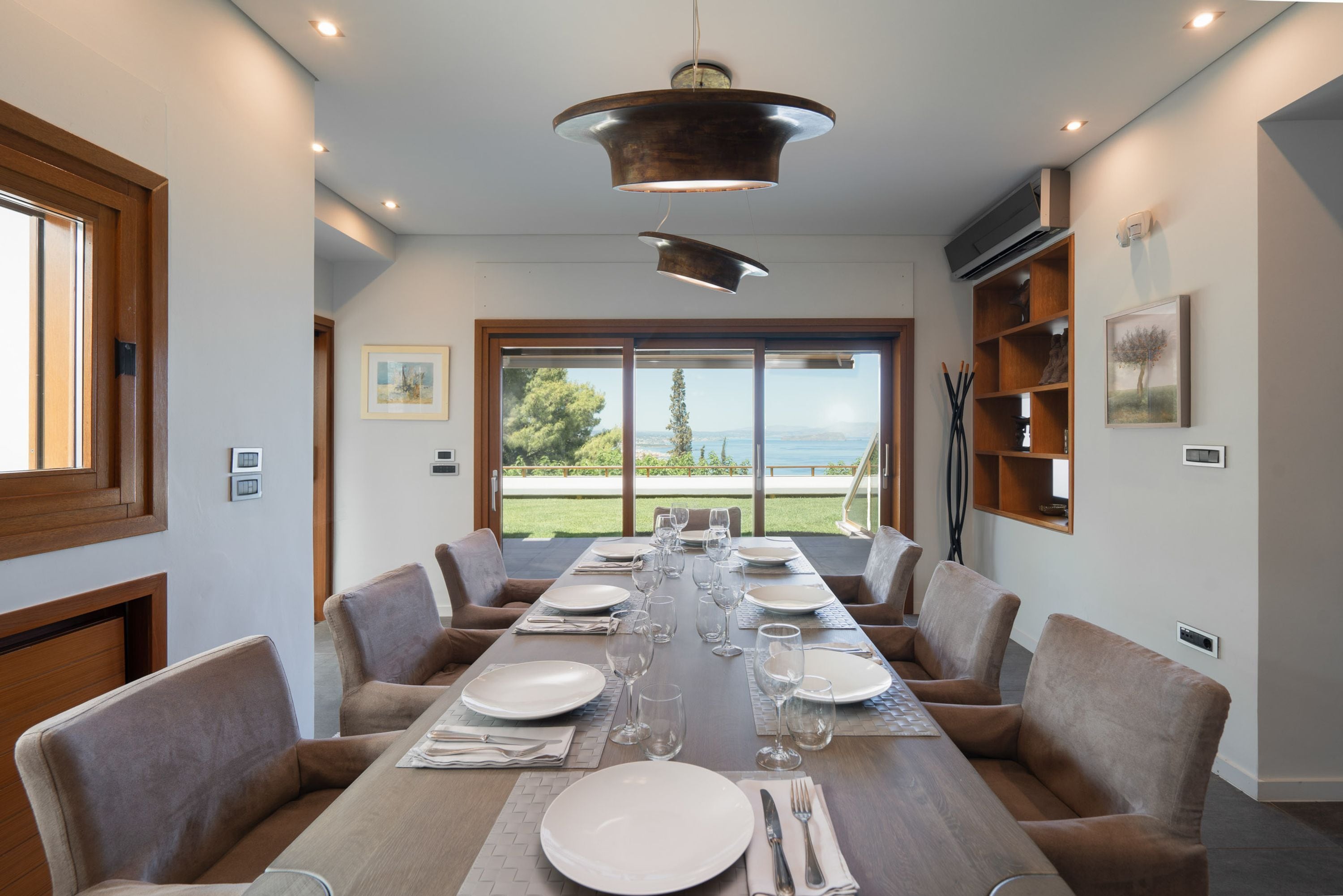 Uma sala de jantar com uma mesa comprida posta para seis pessoas, rodeada por cadeiras, com vista para o exterior.