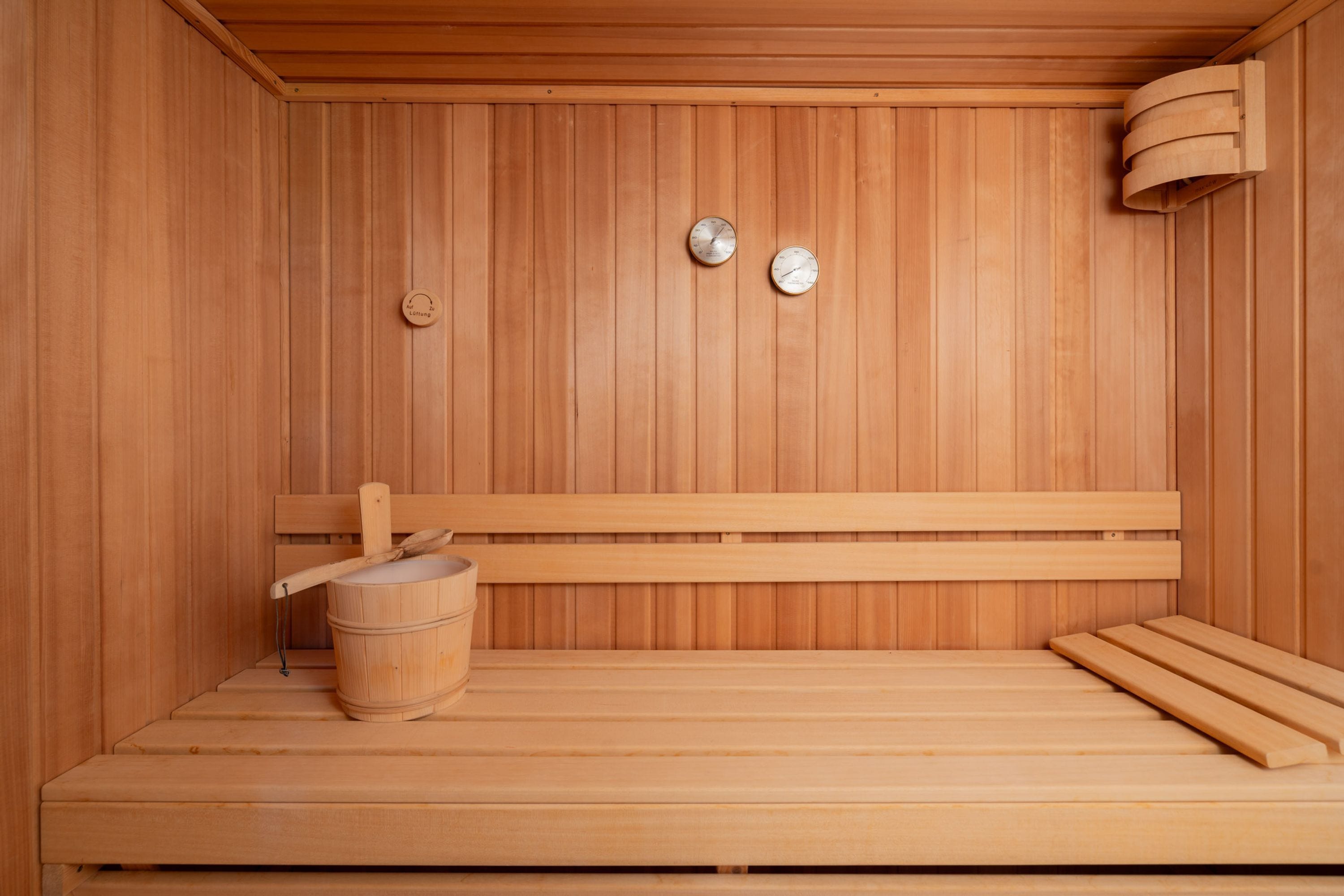 A wooden sauna with benches, a wooden bucket, and two wall-mounted controls.