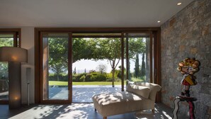 A modern living room with a large sliding glass door leading to a patio, a beige sofa, and a unique wall art piece. - Villa Terra Creta Luxury Retreat and Spa (Chania)