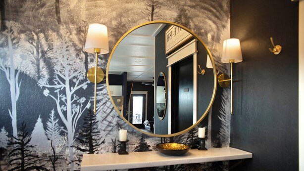 A bathroom with a round mirror, two wall-mounted lamps, a shelf with books, and a decorative wall mural. - Farmhouse outskirts of Norman’s “Okla. University” fastWiFi, 2-75”TVs, KING BED (Noble)