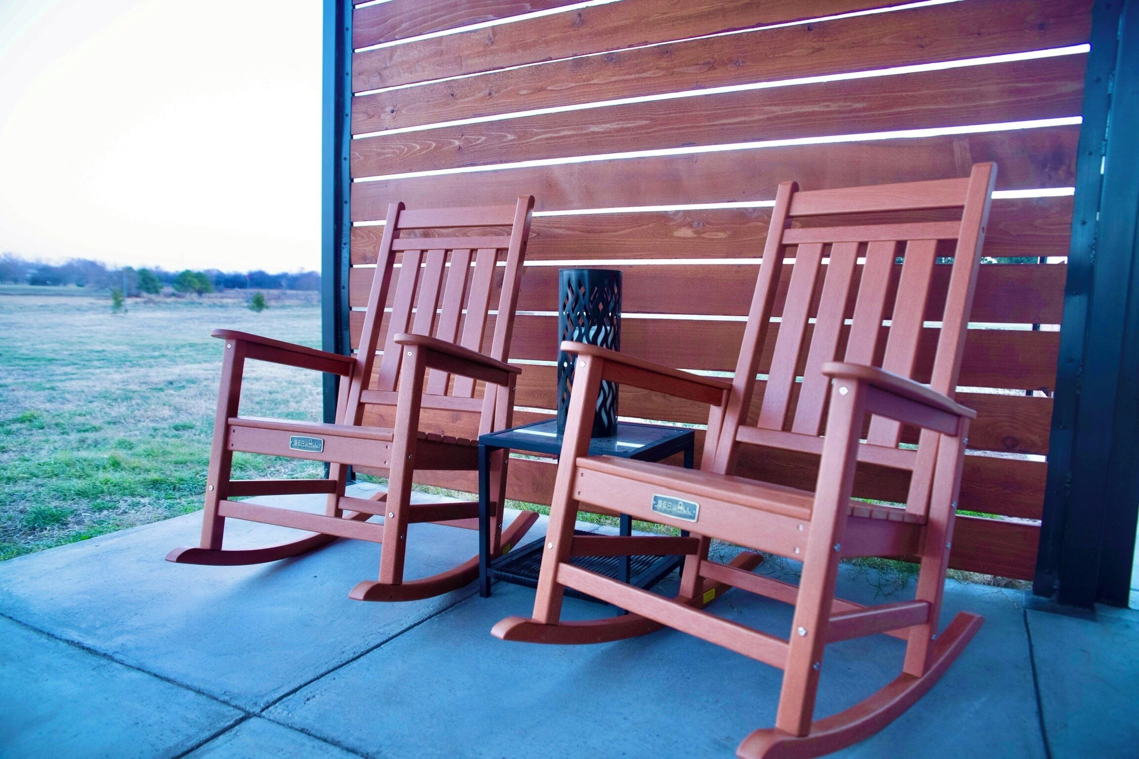 Three rocking chairs in front of a wooden wall with horizontal slats.